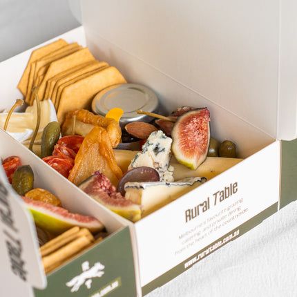 Assorted food items including figs, cheese, and crackers in a 'Rural Table' box.