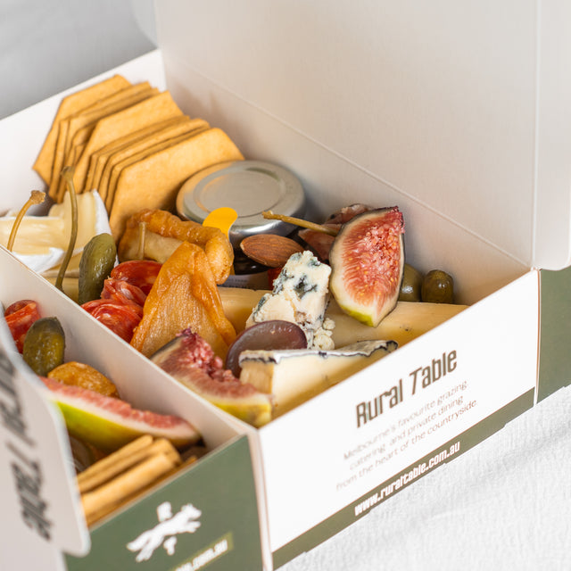 Assorted food items including figs, cheese, and crackers in a 'Rural Table' box.