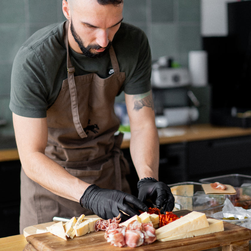 Man in a kitchen preparing food on a wooden board with various ingredients.
