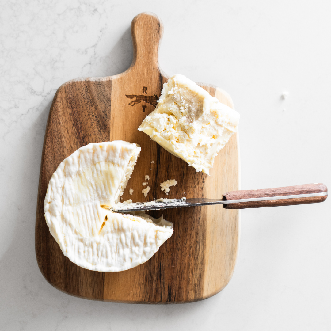 Wooden cutting board with a wheel of cheese and a knife on a light background