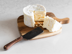 Wheel of soft cheese with a slice removed on a wooden board with a cheese knife.
