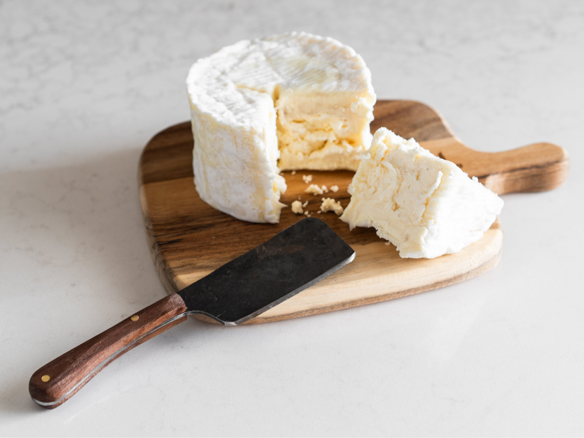 Wheel of soft cheese with a slice removed on a wooden board with a cheese knife.