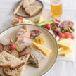 Platter of assorted meats, cheeses, and bread on a white surface with a glass of beer.