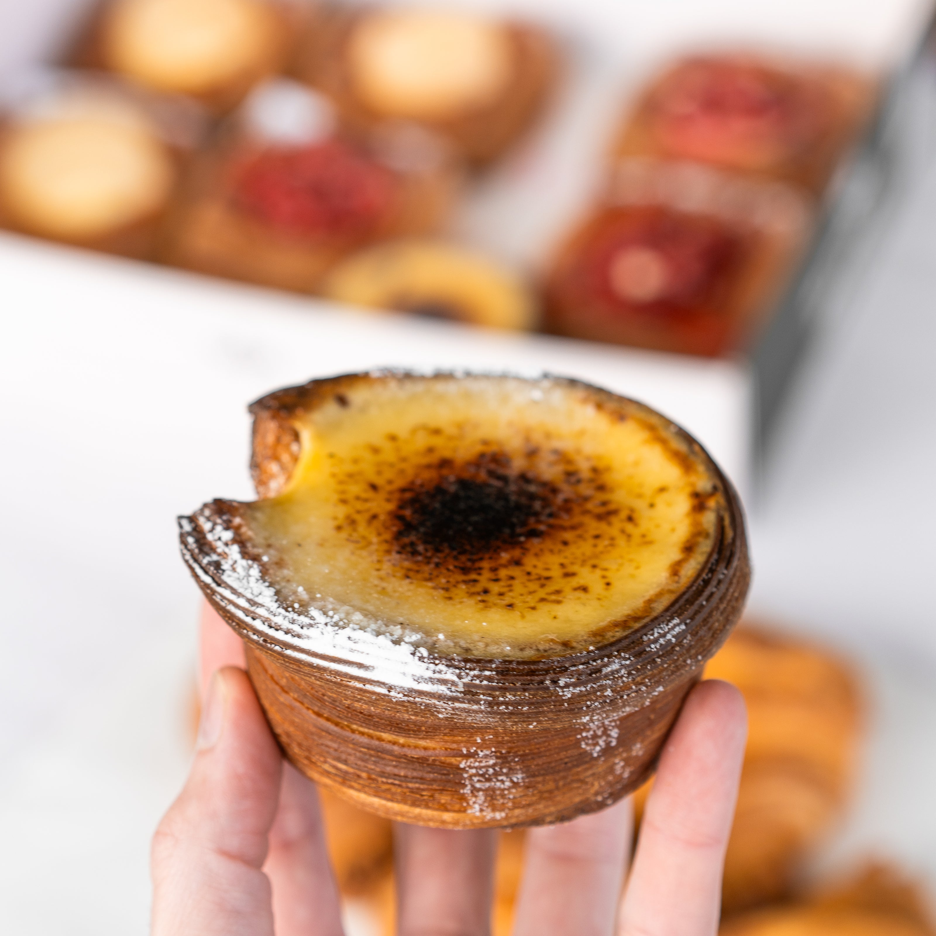 A hand holding a baked pastry with a caramelized top.