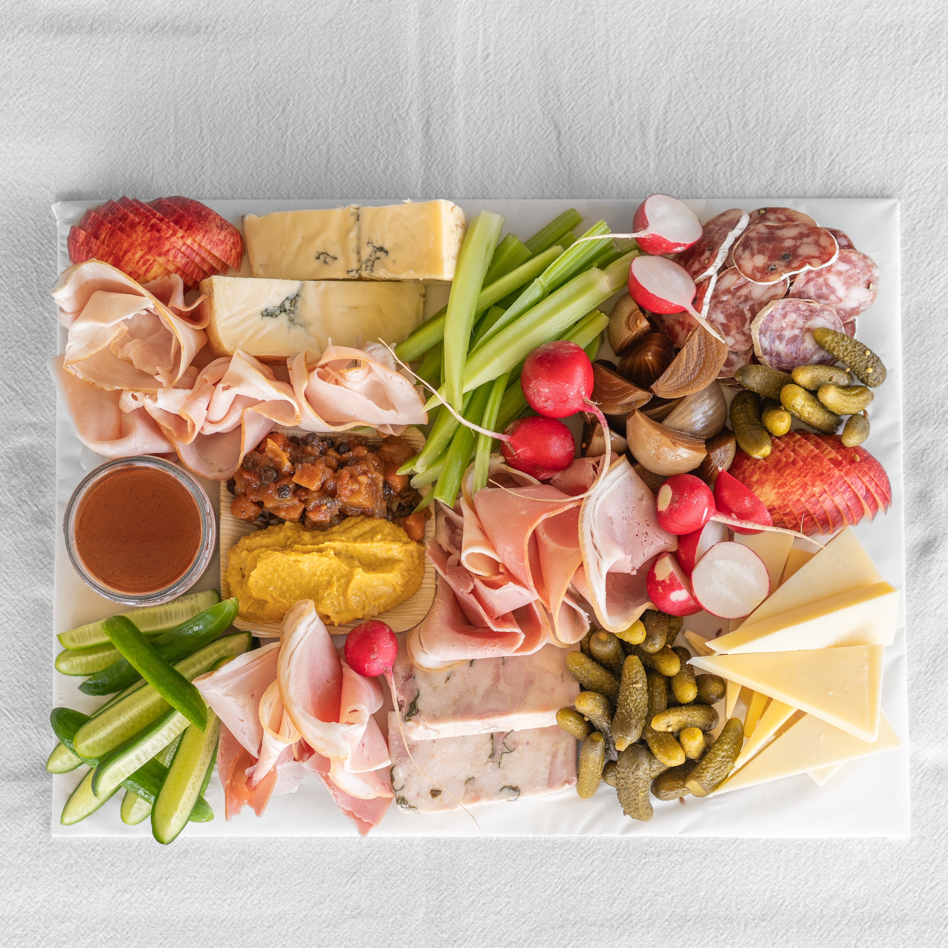 Assorted charcuterie board with meats, cheeses, vegetables, and pickles on a white surface.