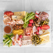 Assorted charcuterie board with meats, cheeses, vegetables, and pickles on a white surface.
