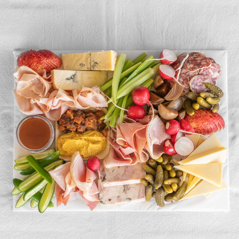 Assorted charcuterie board with meats, cheeses, vegetables, and pickles on a white surface.