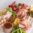 Platter of cured meats, cheeses, and vegetables on a white surface