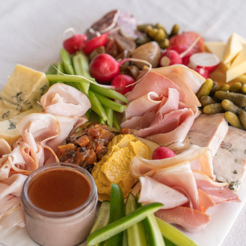Platter of cured meats, cheeses, and vegetables on a white surface