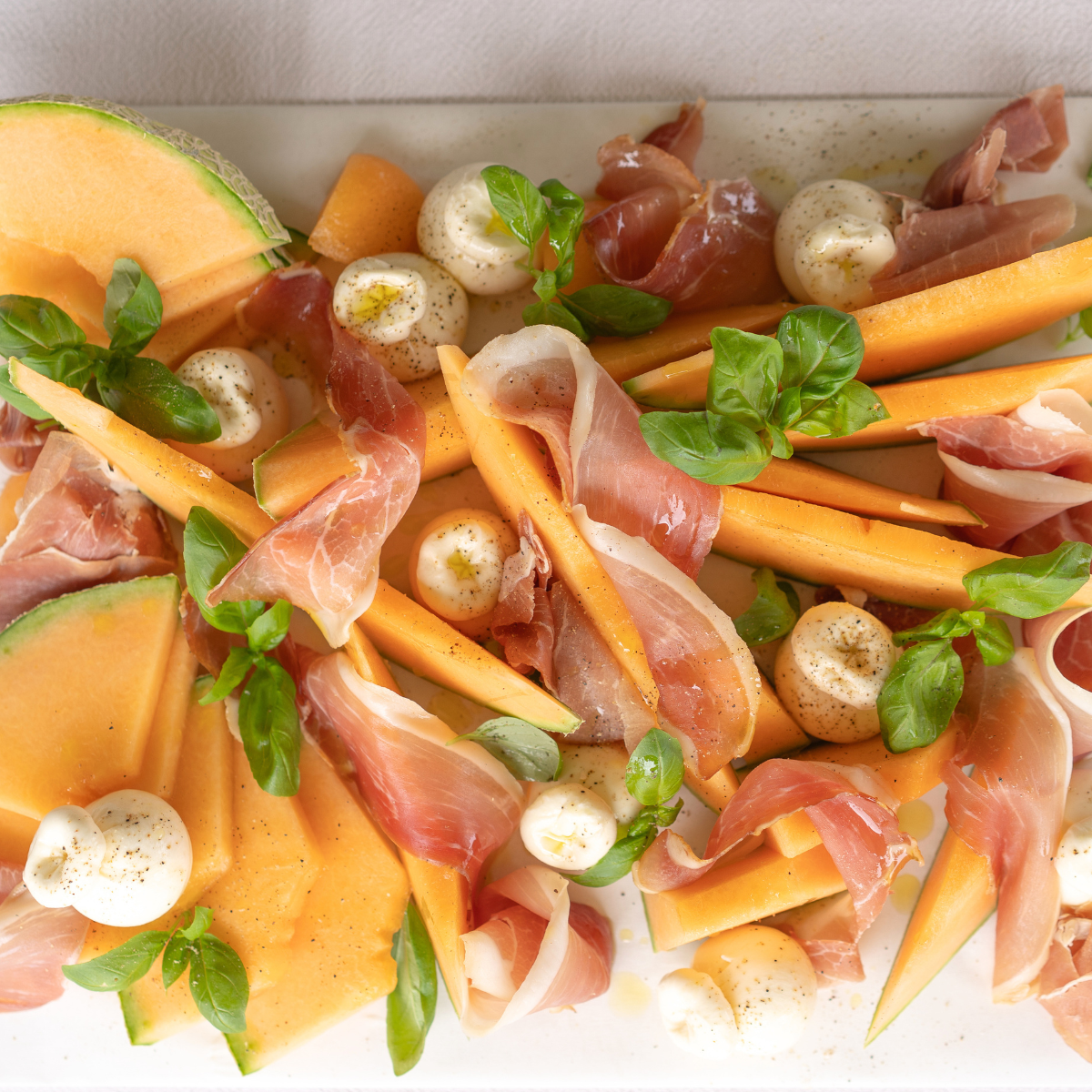 Platter of sliced melon, prosciutto, and mozzarella with fresh basil leaves