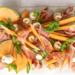 Platter of sliced melon, prosciutto, and mozzarella with fresh basil leaves