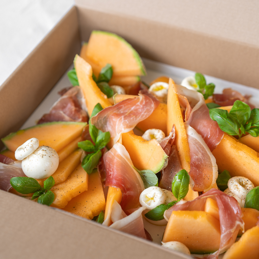 Salad with melon, prosciutto, and mozzarella in a box.